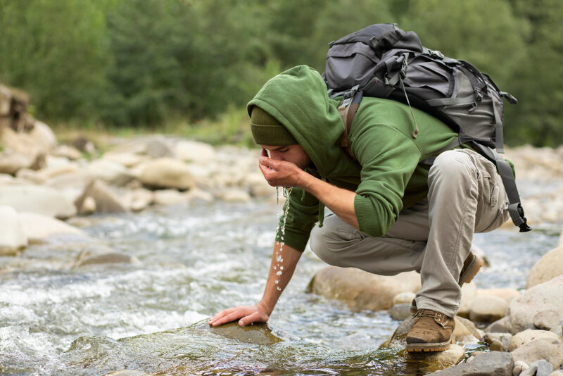 man drinking from a stream